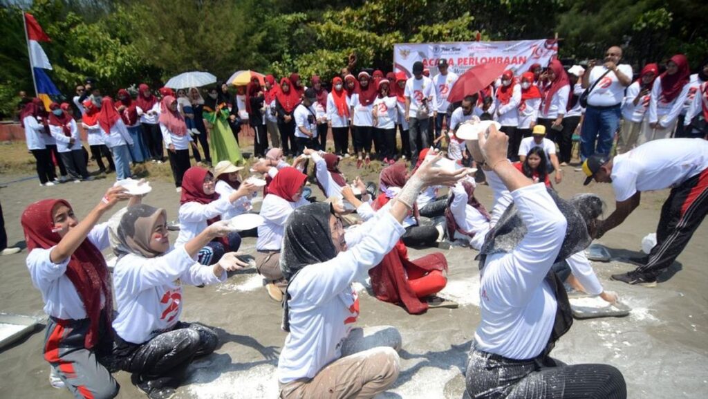 Peserta lomba estafet tepung bekerja sama memindahkan tepung sebagai permainan kelompok yang melatih koordinasi dan kekompakan.